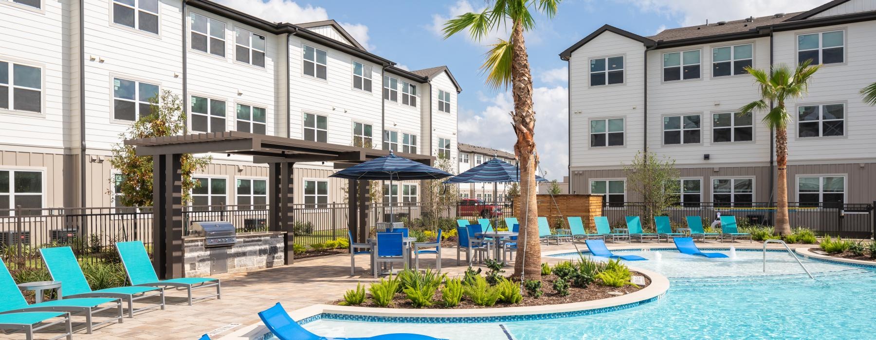 a pool with lounge chairs and umbrellas by a building